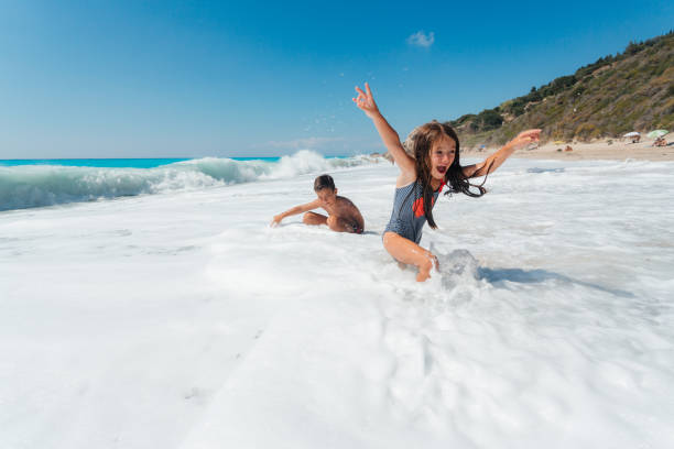 Siblings having fun playing and running in the waves on a beautiful beach on the Greek Lefkada island