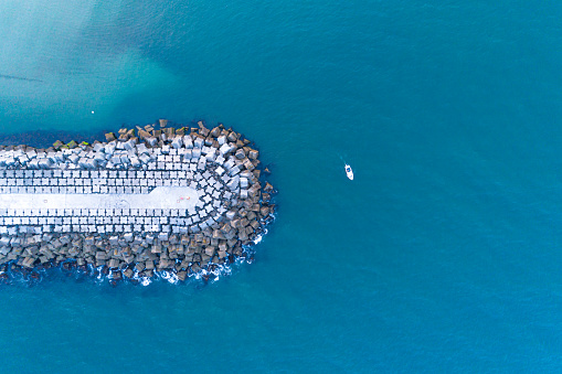 ship sailing near the breakwater of a harbor, top view from a drone
