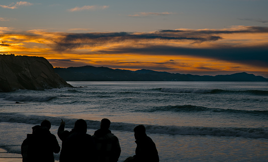 Silhouettes of friends together at the beach, watching the waves under a vibrant sunset sky.