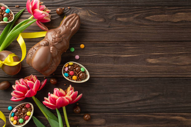 istock Joyful Easter confectionery display. Top view photo showing cracked open chocolate eggs, overflowing with rainbow candies, chocolate bunny, and lively tulips on timber table, blank area for messaging 2084539336