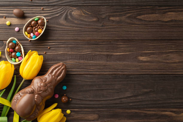 istock Easter delight perspective: top view photograph of chocolate egg broken apart to display assorted candies, alongside a chocolate hare and fresh tulips on a wooden table, with a blank area for text 2084539347
