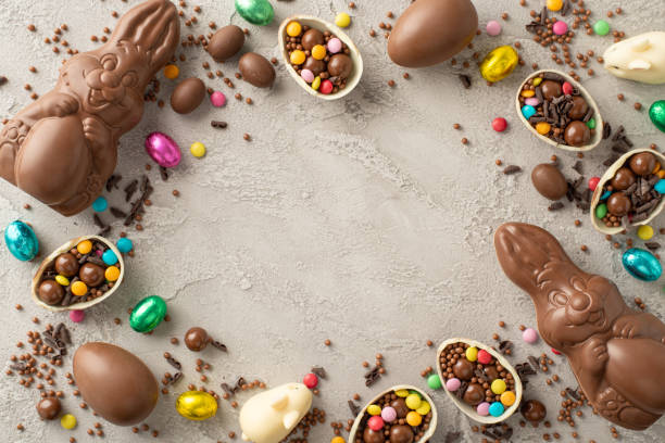 istock Elegant Easter sweets concept. Top view shot of opened chocolate eggs filled with rainbow-colored candies, a sweet chocolate rabbits, sprinkle dots on grey concrete background with space for words 2084539817