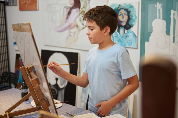 istock Adorable Caucasian child boy holding paintbrush, drawing on canvas in creative workshop or elementary age school 2084572427