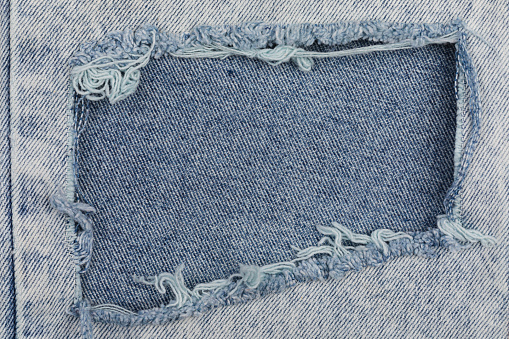 Tear on a worn blue jeans with frayed threads