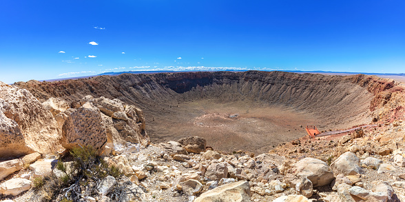 Barringer Meteor crater near Winslow, Arizona; observation platform visible, showing the immense scale. Weathered rocks, desert plants in the foreground. Clear blue sky in above.