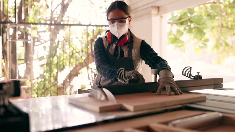 Wood, carpenter and saw with woman in workshop for furniture, manufacturing and renovation. Production, tools and design with person and equipment in home garage for remodeling, board and handyman