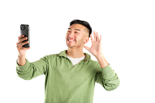 smiling young asian man in green shirt taking a selfie with his smart phone on white background