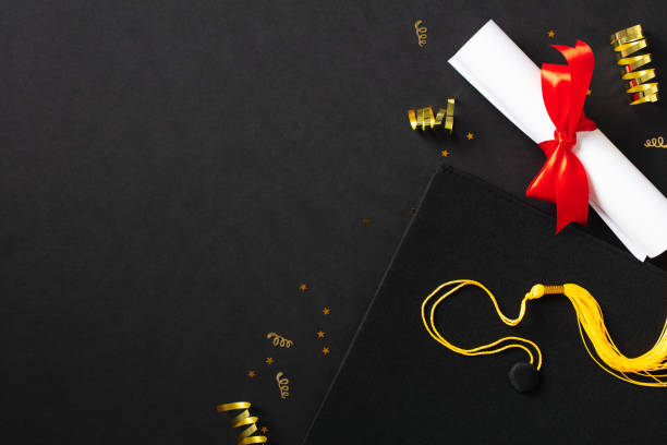 istock Top view graduation mortarboard cap, diploma, gold tinsel on black background. Graduation party, education concept. 2084679237