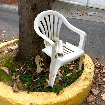 Broken leg of white plastic chair in the street of Caracas city by the side of tree trunk