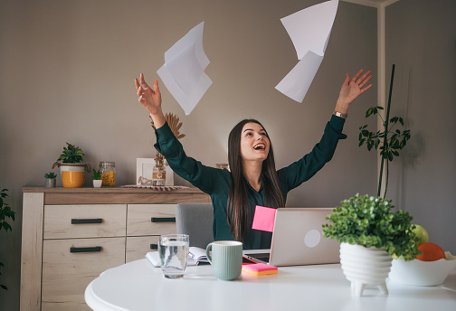 Young business woman doing paperwork at home, she looks very happy and throwing papers after a successful job.