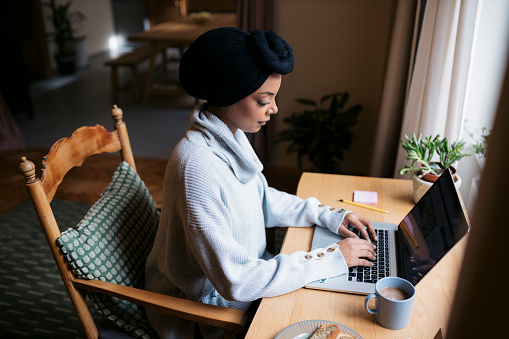 High angle view of a dedicated young woman working at home. Female wearing traditional headwear using laptop sitting at home office desk.