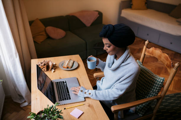 istock Young woman freelancer drinking coffee and working on laptop at home office 2084739410