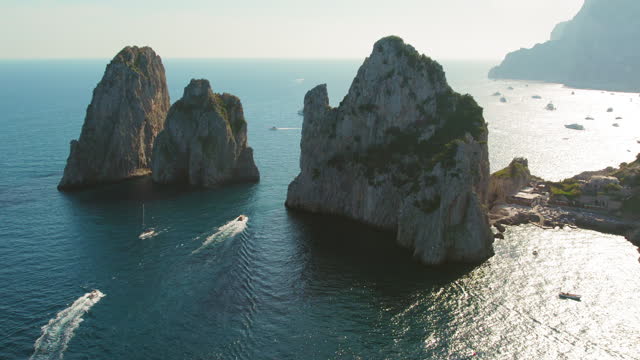 The iconic Faraglioni rocks stand majestically in the Tyrrhenian Sea, surrounded by leisure boats near Capri, Italy, during summer.