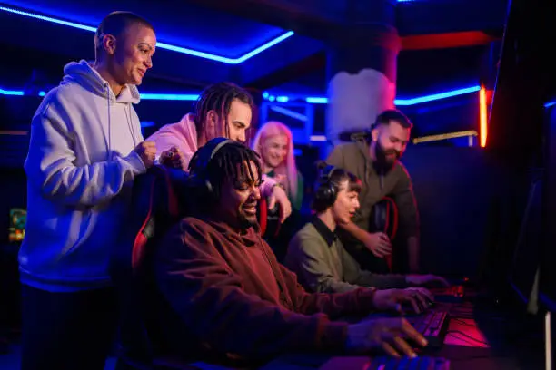 African american male gamer playing PC video game and having fun with his friends. Black male video game player playing with his multiracial team in a Esports arena or on a Gaming convention.