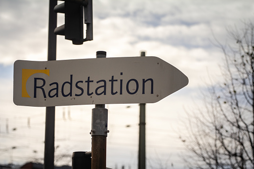 Cologne, Germany - November 6, 2022: Picture of a sign indicating the nearest radstation in Germany. A Radstation, particularly the one in Cologne, serves as a multifaceted facility offering a wide range of services around bicycles. It is a social project aimed at vocational integration and employment development, providing jobs, training positions, and further qualifications for unemployed individuals, with a focus on all aspects of bicycle services. Customers can benefit from services such as bicycle rentals, guided city bike tours, bicycle repairs, and secure parking. Additionally, it operates with an emphasis on social participation, environmental protection, and promoting healthy activity.