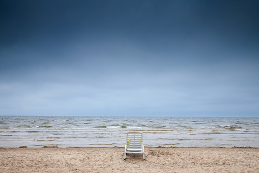 Panorama of an empty plastic lounge chair in Jurmala beach (Jurmalas Pludmale) in Dubulti, Latvia, on baltic sea, on a rainy foggy cloudy afternoon. Jurmala is a sea resort of Latvia in baltic states.