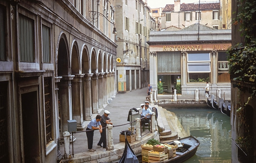 Morning street scene along the Venice, Italy canals with fresh vegetables being delivered by boat and parked gondolas. Photo taken August 28, 1967.