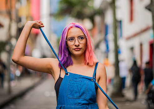 portrait of a young woman walking through the streets of the city while her hands play with the straps of her oberol.