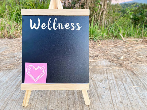 Healthy Lifestyle Concept - Wellness word and heart shape on whiteboard with nature background. Stock photo.