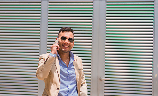 executive man smiling while wearing his glasses and using his cell phone walking down the street
