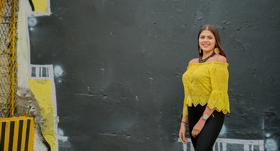 young latin woman smiling and looking at the camera while wearing a yellow blouse and strolling through the streets of the city.