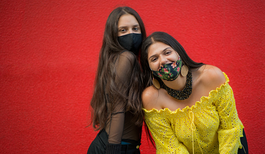 woman wearing masks while standing on a red background and one of them smiling happily