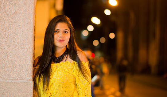 latina woman with long hair in the city at night and wearing colourful clothes while smiling