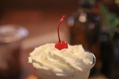 Whipped cream with a red candied cherry on top in cafe or restaurant. Natural milk desserts. Appetizing Cake or dessert.
