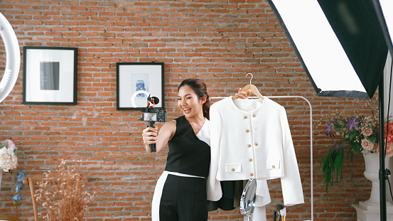 Woman influencer shoot live streaming vlog video review clothes social media or blog. Happy young girl with apparel vivancy studio lighting for marketing recording session broadcasting online.