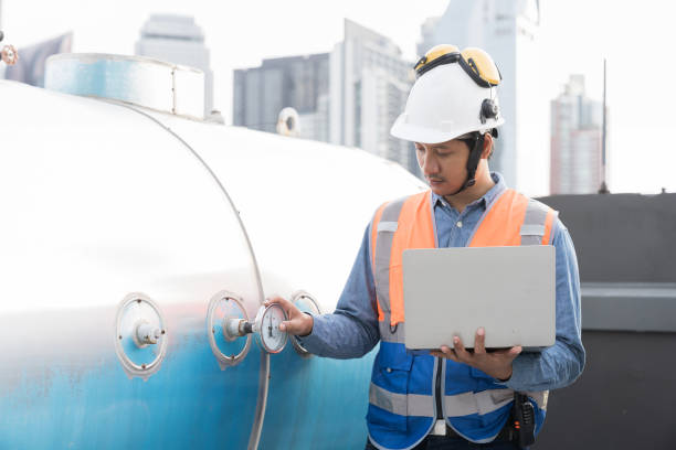istock Asian male engineer working using laptop computer checks water tank at construction site. Male engineer inspecting water tank pressure. Asian male plumber worker maintenance water tank pressure system 2084960925