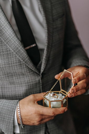 Close-up of a glass box with wedding rings in the hands of the groom. Data about the groom