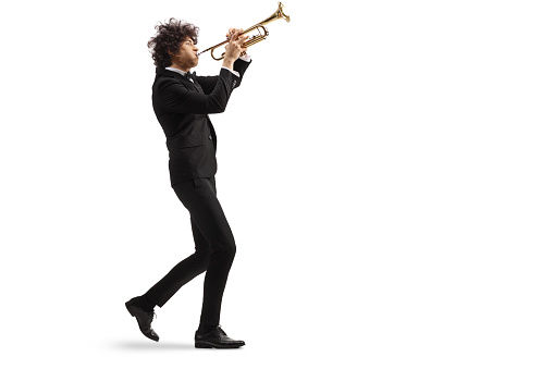 Male musician in a black suit walking and playing a trumpet isolated on white background