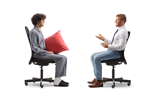 Profile shot of a businessman sitting in an office chair and talking to a man in pajamas isolated on white background