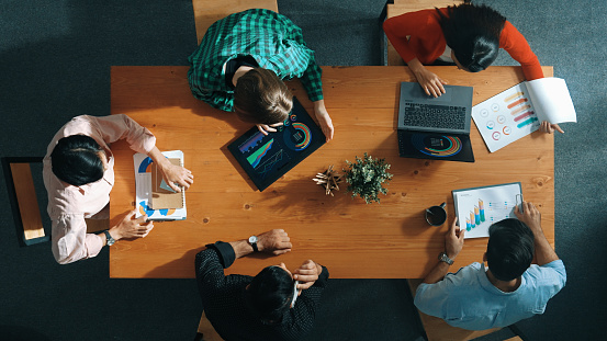 Top down view of manager holds tablet display increasing sales and placed on meeting table. Group of diverse business team clapping hands to celebrate successful product at meeting room Convocation.