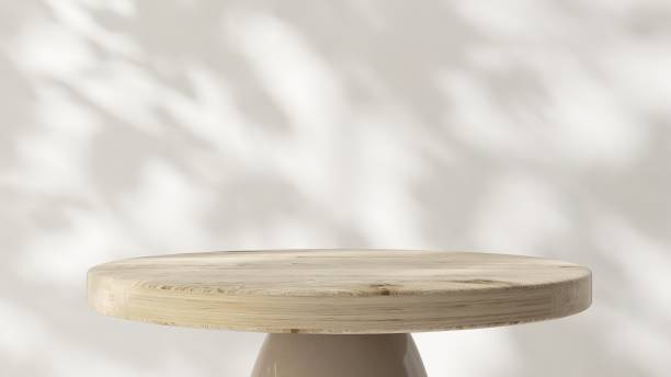 istock Round wooden pedestal table podium in dappled sunlight, leaf foliage shadow on white wall 2085012680