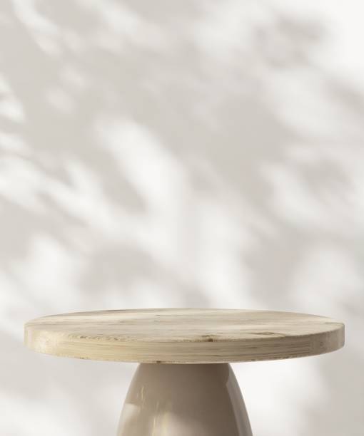 istock Round wooden pedestal table podium in dappled sunlight, leaf foliage shadow on white wall 2085013196