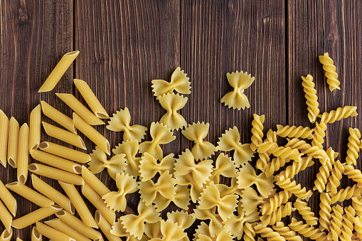 Different kinds of raw pasta texture with copy space on wooden background. Top view of Italian cuisine ingredient.