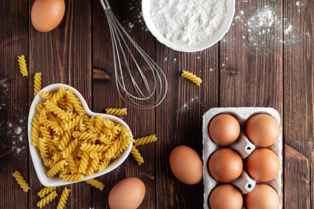 Raw pasta fusilli with eggs on wooden background. Top view of Italian cuisine ingredient.