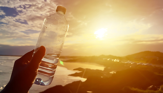 woman hand holding water bottles with sunset light effect background.