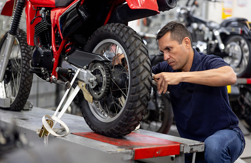 Latin American mechanic installing a tire on a motorcycle at a repair shop - vehicle breakdown concepts