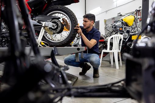 Latin American mechanic installing a wheel on a motorcycle at a repair shop - vehicle breakdown concepts