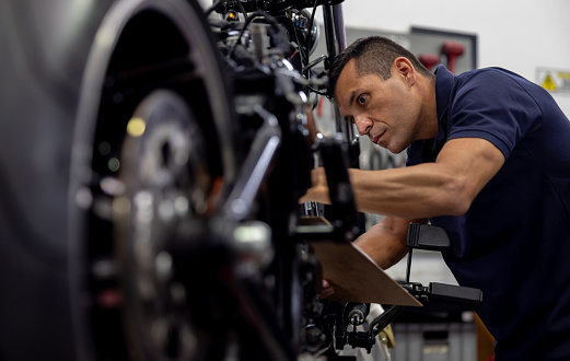 Latin American mechanic repairing a motorcycle at a repair shop - vehicle breakdown concepts