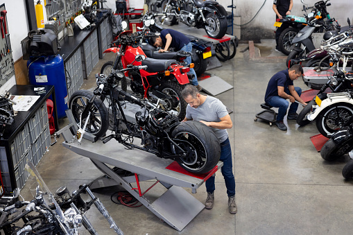 Team of Latin American mechanics fixing motorcycles at a garage - vehicle breakdown concepts