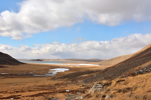 View of the valley sandwiched in the mountains to the frozen river flowing into the picturesque lake in the autumn steppe.
