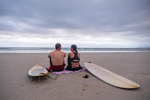 Rear view of a young couple sitting together on the beach with their surfboards after a great surf session