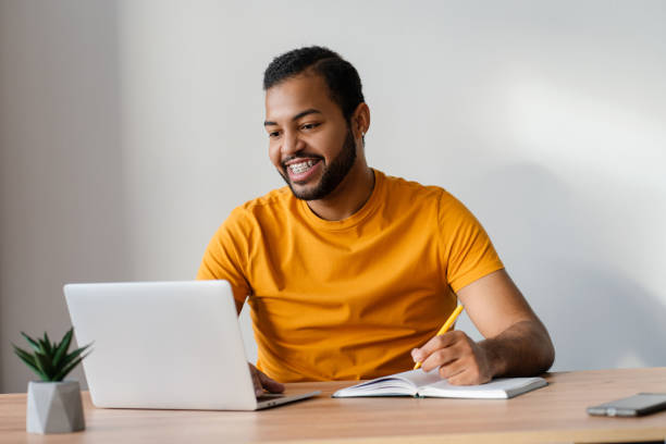 istock Smiling african american man with dental braces on teeth using laptop computer studying 2085204738