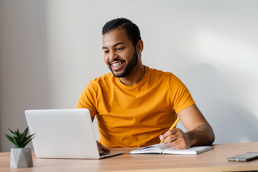 Smiling african american man with dental braces on teeth using laptop computer studying, learning language. Technology, online education concept