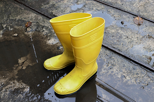 Photo of yellow rubber boots in a puddle of water, these shoes are usually worn by workers and farmers, these boots are waterproof