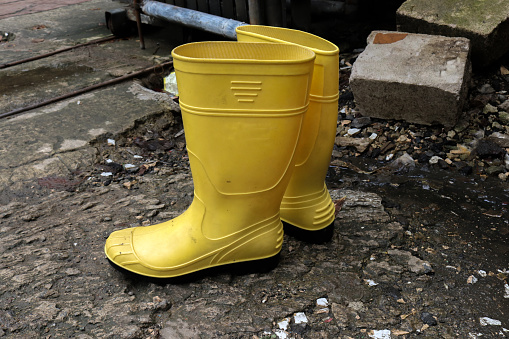 Photo of yellow rubber boots on a pile of rubbish, these shoes are usually worn by workers and farmers, these boots are waterproof