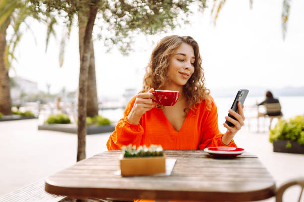istock Young woman at summer cafe drinking coffee and using mobile phone. 2085244030